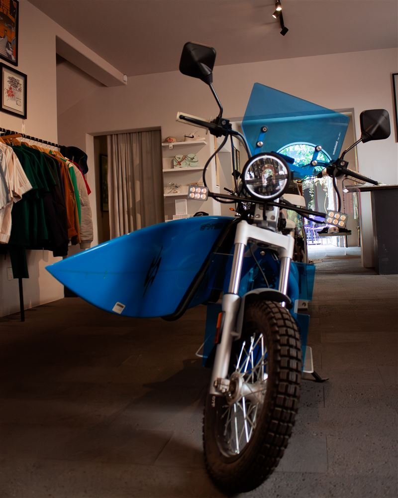 Motocicleta azul exhibida dentro de una tienda, con ropa colgada al fondo.