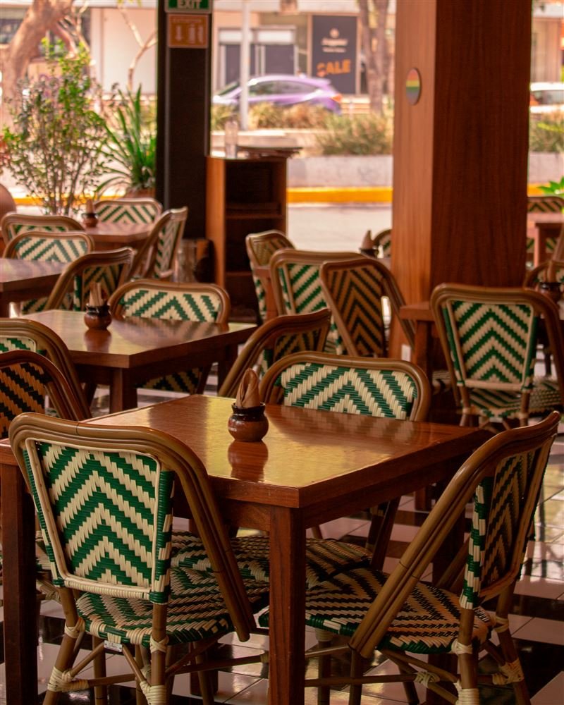 Terraza de restaurante con mesas de madera y sillas de mimbre en verde y blanco.